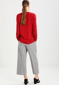 Haut rouge à manches longues avec une coupe décontractée, associé à un pantalon gris à jambes larges. Une paire de chaussures à talons carrés noires complète la tenue.