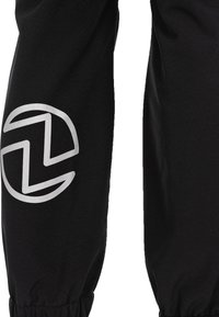 Schwarze Sporthose mit einem silbernen Logo an der unteren Beinpartie, hergestellt aus einem glatten, dehnbaren Stoff mit gerafften Bündchen.