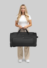 Schwarze Duffle-Tasche mit einer glatten, strukturierten Oberfläche, zwei stabilen Griffen und einer vorderen Reißverschlusstasche, vor einem grauen Hintergrund präsentiert.