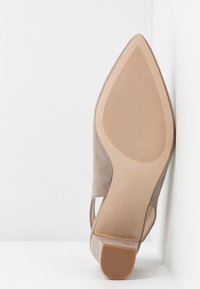 Beige mockask klackskor med spetsig tå, texturerad sula och låg klack, storlek 5, placerad med sulan upp mot vit bakgrund.