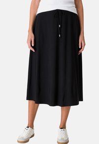 Jupe noire longueur genou en tissu doux ; taille réglable avec cordon et finitions argentées. Associée à des baskets blanches.