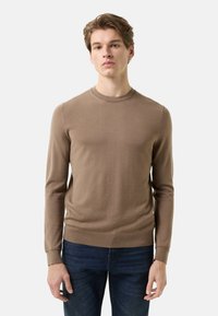 Brown long-sleeve sweater in soft knit fabric, featuring a crew neck, ribbed cuffs, and a slim fit. Worn with dark jeans.