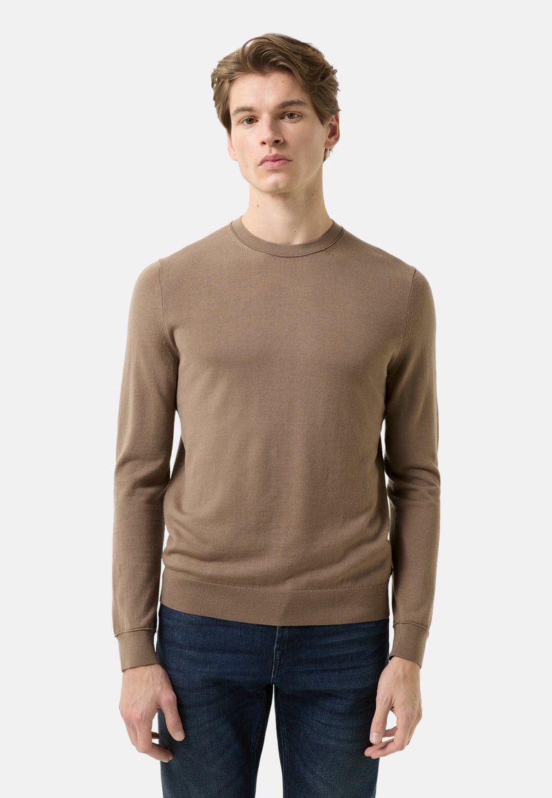 Brown long-sleeve sweater in soft knit fabric, featuring a crew neck, ribbed cuffs, and a slim fit. Worn with dark jeans.