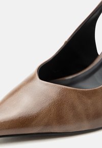 Καφέ δερμάτινο παπούτσι μπαλαρίνα με μυτερή μύτη, χαμηλό κόψιμο και μαύρη εσωτερική επένδυση σε λευκό φόντο.