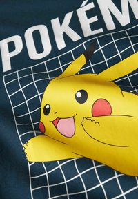 Navy blue cotton t-shirt featuring a large yellow Pikachu graphic on a grid background, with the word "POKÉMON" above in white.