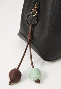 Sac en cuir noir texturé avec fermeture éclair, orné de deux cordons décoratifs : une boule en laine marron et une autre en laine vert menthe.