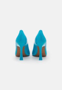 Niebieskie lakierowane szpilki z wąskim noskiem, wysokim obcasem typu stiletto oraz naturalnym drewnianym akcentem u podstawy obcasa.