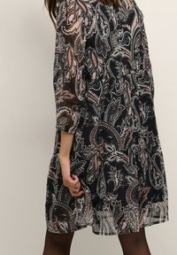 Black, sheer dress with a paisley print in shades of pink and grey. Features three-quarter sleeves and a flowy, tiered design.