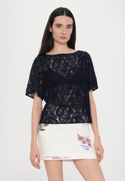 Navy lace top with short sleeves and floral patterns, paired with a white mini skirt featuring colorful embroidery and decorative stitching.