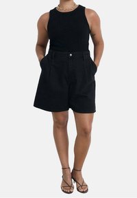 Top negro sin mangas combinado con pantalones cortos de mezclilla negros de cintura alta, que cuentan con bolsillos frontales, cierre de botón y un corte relajado.