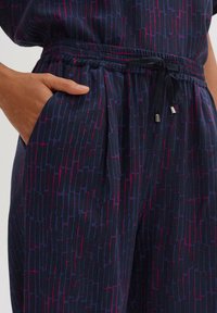 Navy-gepatroneerde broek met een gestructureerd abstract ontwerp in paars en roze, voorzien van een elastische tailleband en een trekkoord met metalen punten.