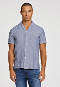 Korte mouwen shirt in lichtblauw linnenmengsel met een kraag, vijf knopen en subtiele textuur. Gecombineerd met donkere spijkerbroek.