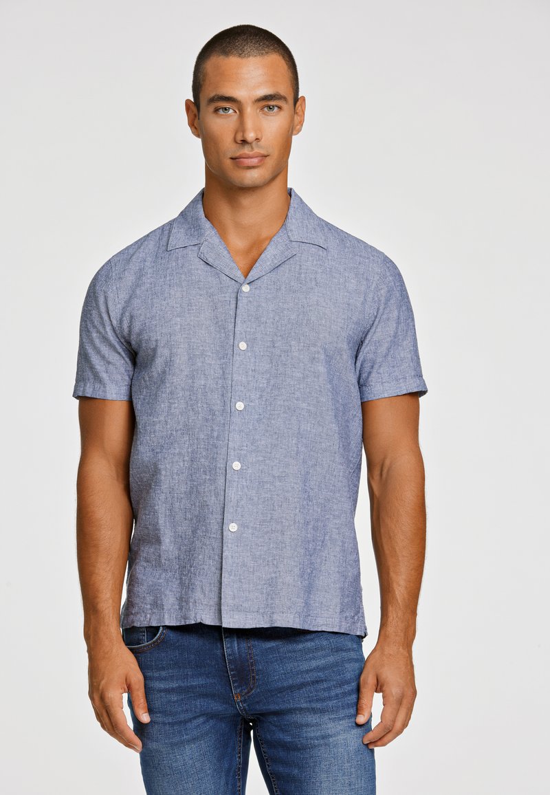 Korte mouwen shirt in lichtblauw linnenmengsel met een kraag, vijf knopen en subtiele textuur. Gecombineerd met donkere spijkerbroek.