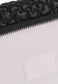 Parte superiore in pelle nera testurizzata con parte inferiore in canvas rosa, caratterizzata da una zip argentata e un'etichetta in rilievo rosa "TOUS".