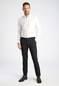 Biała koszula zapinana na guziki z kieszonką, w połączeniu z czarnymi spodniami o wąskim kroju i czarnymi eleganckimi butami. Prosty design, gładka faktura, dopasowany krój.
