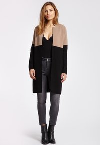 Long cardigan beige et noir, en matériau doux. Ouverture à l'avant sans fermetures, avec des manches longues et une coupe droite.