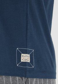 Tamno plava pamučna majica s kvadratnom etiketu našivenom na donjem lijevom dijelu, s natpisom "BLEND 1993 DENIM WITH ATTITUDE" u krem boji.