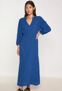 Robe longue bleue avec un décolleté en V, des manches bouffantes élastiques et une taille cintrée. Fabriquée en tissu léger, elle présente une silhouette fluide.