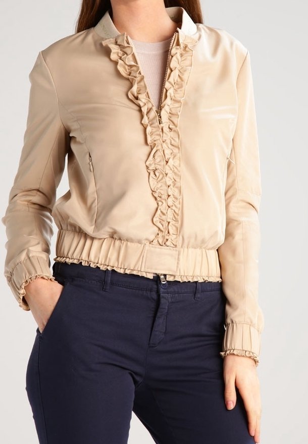 Veste en simili cuir beige avec des volants le long du plastron et des poignets, taille élastique et manches longues, dotée d'une fermeture éclair.