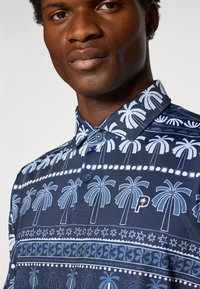 Polo a maniche corte di colore blu navy con motivo di palme e righe decorative. Include un colletto button-down e ricami discreti.