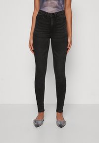 Svarte høyt midjebukser i skinny fit med teksturert stoff, som har en tettsittende silhuett og subtil fading. Båret med grå spisse sko.