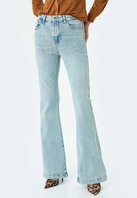 Vaqueros de campana azul claro hechos de denim con un lavado desgastado, con cierre de botón, cinco bolsillos y detalles de costura a lo largo de las costuras.