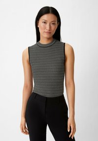 Schwarz-weiß gestreifter ärmelloser Oberteil mit hohem Halsauschnitt, aus einem gerippten Strickstoff gefertigt, kombiniert mit schwarzen maßgeschneiderten Hosen.