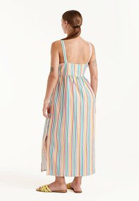 Vestido maxi a rayas con tirantes finos, que presenta líneas verticales multicolores sobre un fondo blanco, y una abertura lateral para mayor facilidad de movimiento.