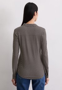 Camisa de manga larga con una base marrón oscuro y un patrón geométrico blanco. Tejido suave con un dobladillo curvado y silueta ajustada.