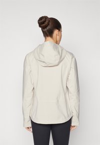 Helle beige Kapuzenjacke mit langen Ärmeln, glattem Stoff und lockerer Passform. Verfügt über verstellbare Kordelzüge und seitliche Schlitze.