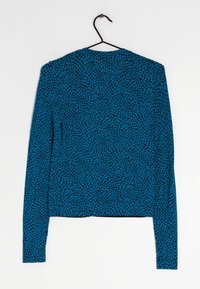 Dlouhý rukáv top s texturovanou modrou tkaninou a černým abstraktním vzorem, kulatým výstřihem a zkrácen�ým lemem. Visí na háčku.