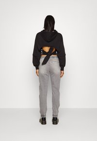 Sudadera negra corta con un detalle de lazo en la parte trasera, combinada con pantalones grises ajustados y botas negras gruesas. Textura suave, diseño casual.