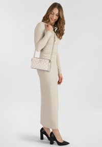 Abito aderente beige con maniche lunghe e scollatura rotonda, abbinato a una borsa a tracolla rosa chiaro con motivo e scarpe con tacco quadrato nere.