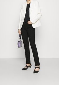 Vit skräddarsydd kavaj över en svart topp, i kombination med svarta jeans och svarta slingback-klackar. Håller en liten lila handväska.