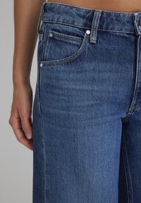 Blue denim jeans with a classic design, featuring a button closure, front pockets, and visible stitching. The fabric has a soft, textured finish.