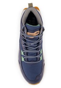 Zapatilla deportiva azul marino con acentos verdes, collar acolchado gris y tirador marrón; etiqueta "Fresh Foam" en la lengüeta y cordones redondos.