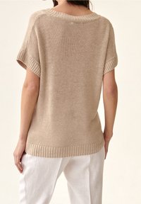 Béžový pletený svetr s krátkými rukávy, širokým výstřihem, žebrovanými manžetami a spodním lemem. Texturovaná látka kontrastuje s hladkými bílými kalhotami.