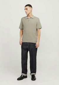 Siva polo majica s kratkimi rokavi, teksturiran material in ovratnik, v kombinaciji z temnimi denim hlačami, zavihanimi na manšetah, in črnimi čevlji.