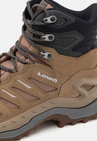 Brauner Wanderschuh aus Wildleder und Mesh-Material, mit grauen Akzenten, einer robusten Sohle und verstärkten Ösen für die Schnürsenkel. Logo sichtbar.