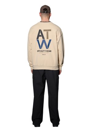 Crème sweatshirt met grote blauwe en bruine grafische tekst op de achterkant, gecombineerd met zwarte cargobroek. De tekst bevat "OFF DUTY GEAR" en "HALO."