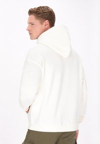 Hvid hættekn�æde med snøre, ribbede manchetter og kant. Stoffet ser blødt ud, har en afslappet pasform og et minimalistisk design.