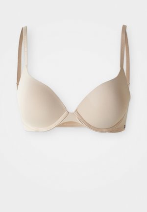 Nježni bež grudnjak s podstavom, s potporom od žica i podešivim naramenicama, s diskretnim natpisom brenda na bijeloj pozadini.
