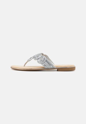 Flat sandal with tan sole and silver braided straps featuring circular decorative patterns on a plain white background.
