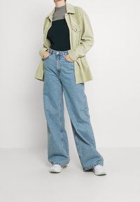 Grünes Cordhemd, dunkelgrünes Ribber-Top, lockere hellblaue Jeans und weiße Sneakers mit grünen Akzenten. Schlichtes Design, lässige Passform.