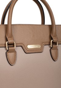 Torebka w kolorze brązowym o fakturze, z podwójnymi uchwytami na górze, złotymi akcentami sprzętu oraz emblematem z logo. Posiada strukturalny design oraz szczegółowe przeszycia.