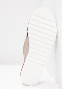Schuh mit einem strukturierten beigen Obermaterial und einer weißen Gummisohle. Die Sohle weist horizontale Rillen für einen besseren Halt auf, und das Design ist minimalistisch.
