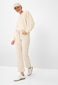 Felpa beige con maniche a palloncino, abbinata a pantaloni slim-fit beige chiaro con cuciture laterali. Sneakers bianche con suola marrone.