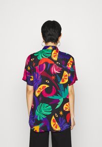 Camicetta a maniche corte con un vivace motivo tropicale di foglie e frutti, su uno sfondo nero. Tessuto morbido con una vestibilità comoda.