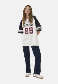 Balta per didelė marškinė su juodomis rankovėmis ir bordo spalvos "BOSTON 89" spauda. Suderinta su tamsiomis džinsinėmis kelnėmis ir baltomis sportinėmis bateliais su pilkais akcentais.