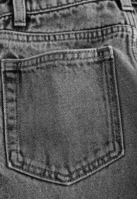 Gros plan de la poche arrière et des détails de couture sur un tissu en jean gris.